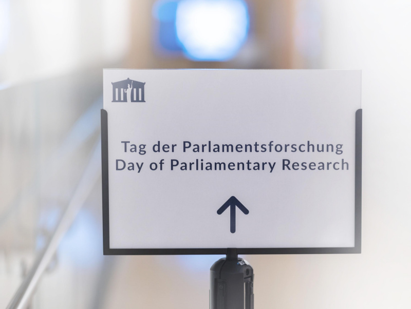 Am Foto ist eine Tafel zu sehen, auf der steht: Tag der Parlamentsforschung und in englischer Sprache Day of Parliamentary Research