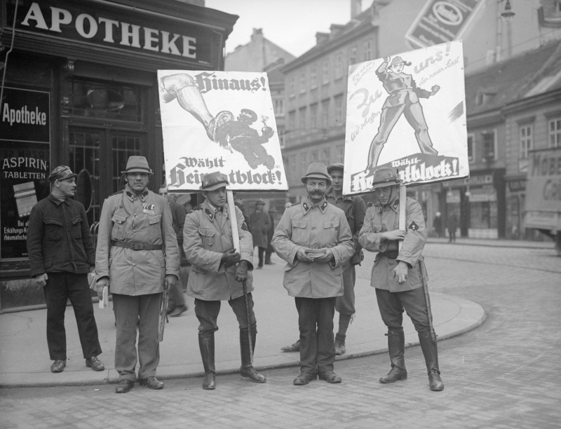 Uniformierte Mitglieder der Heimwehr mit Wahlplakaten.