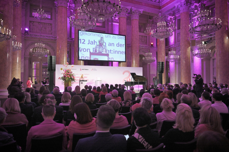 Am Rednerpult Alexandra Schrefler-König. Blick Richtung Veranstaltungsteilnehmer:innen