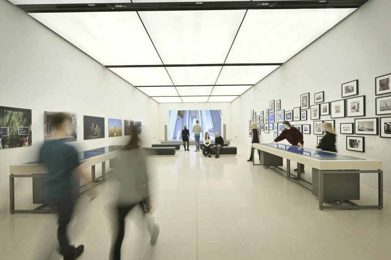 Auditorium: Blick auf die Medientische "Medien und Demokratie" und "Plattformen – Die neuen Öffentlichkeiten im Internet", die LED-Wand sowie die Fotoausstellungen "Global Peace Photo Award" (links) und "Zeitzeugen". Besucher:innen