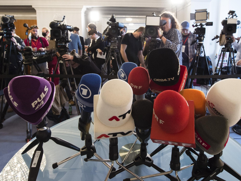 Zahlreiche Journalist:innen mit Kameras und einige Mikrofone auf einem Tisch