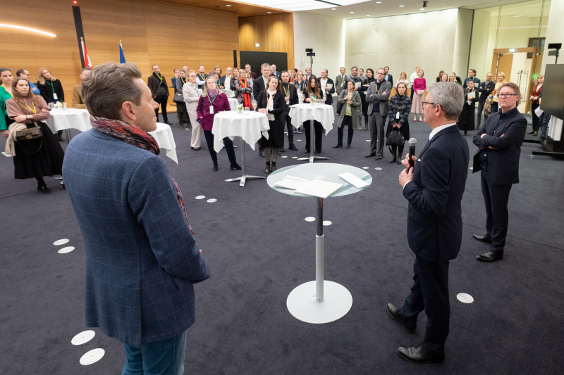 Blick Richtung Veranstaltungsteilnehmer:innen. Eröffnungsworte von Parlamentsvizedirektor Alexis Wintoniak (Mitte), Kurator Kunst im Parlament Hans-Peter Wipplinger -  Leopold Museum (rechts) und Wirtschaftskammerpräsident Harald Mahrer - WKÖ (links)
