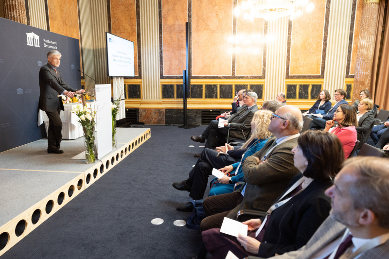 Blick Richtung Veranstaltungsteilnehmer:innen. Am Rednerpult: Parlamentsdirektor Harald Dossi