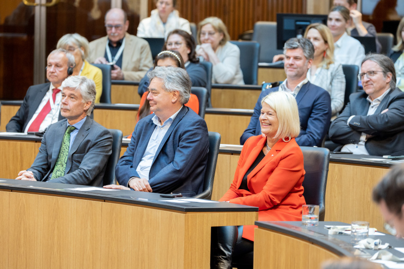 Blick Richtung Veranstaltungsteilnehmer:innen. Von links: Eröffnungsworte von Parlamentsdirektor Harald Dossi, Vizekanzler Werner Kogler (GRÜNE), Verteidigungsministerin Klaudia Tanner (ÖVP)