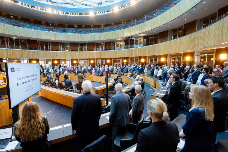Die Veranstaltungsteilnehmer:innen erheben sich zur Bundeshymne
