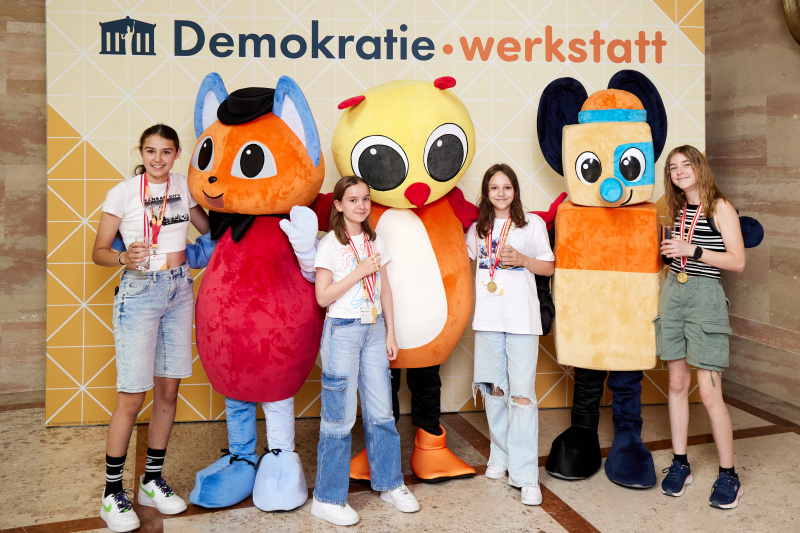 Fotopoint mit den Maskottchen der Demkratiewerkstatt und Schüler:innen