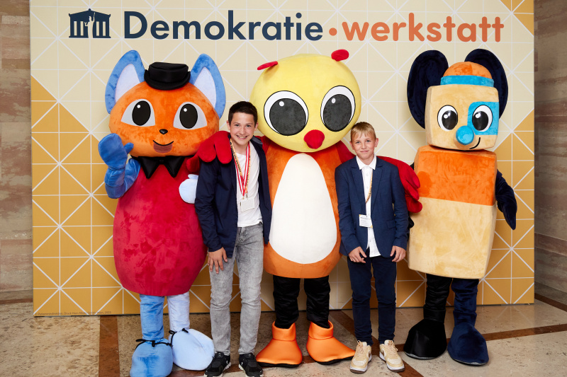 Fotopoint mit den Maskottchen der Demkratiewerkstatt und Schüler:innen