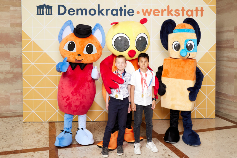 Fotopoint mit den Maskottchen der Demkratiewerkstatt und Schüler:innen