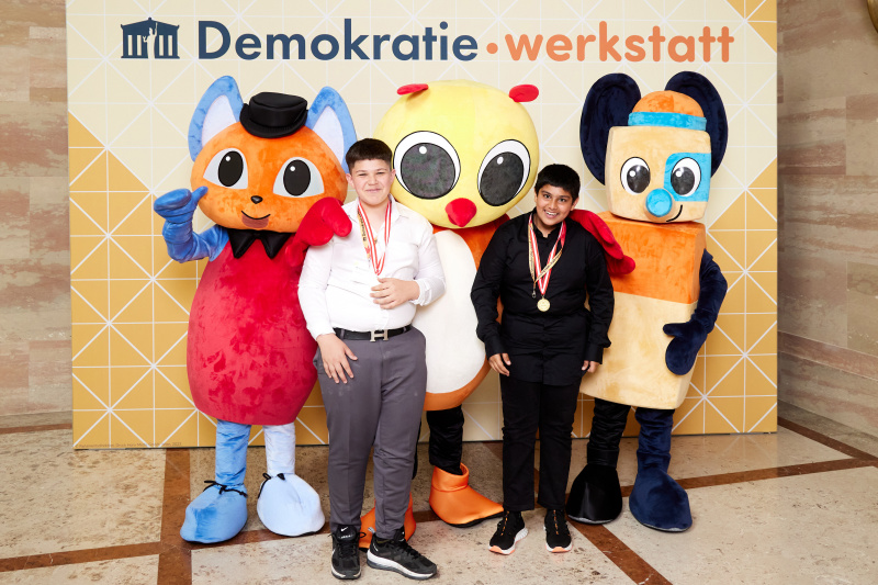 Fotopoint mit den Maskottchen der Demkratiewerkstatt und Schüler:innen