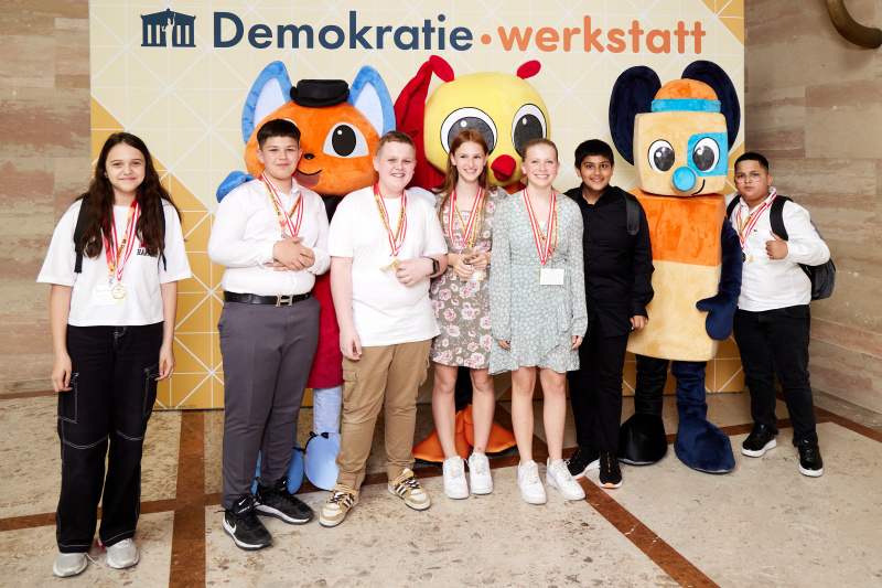 Fotopoint mit den Maskottchen der Demkratiewerkstatt und Schüler:innen