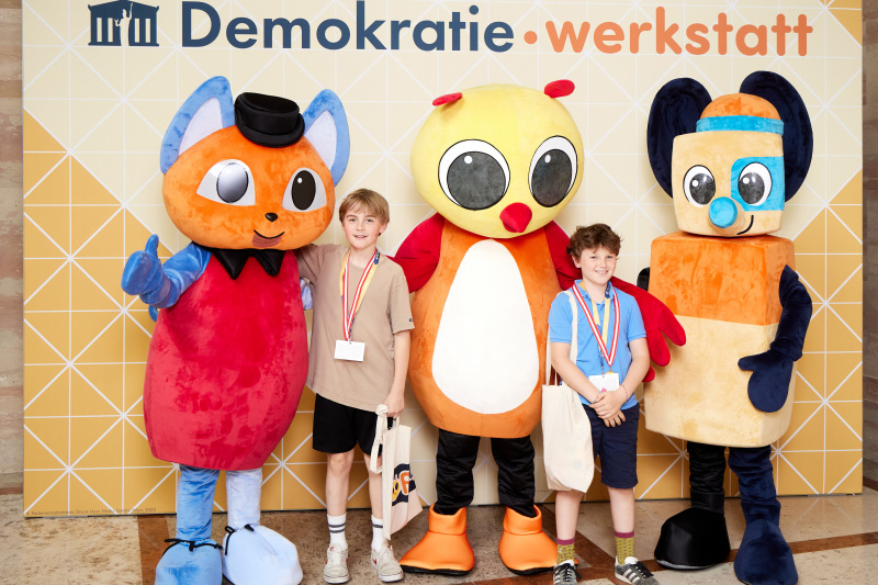 Fotopoint mit den Maskottchen der Demkratiewerkstatt und Schüler:innen