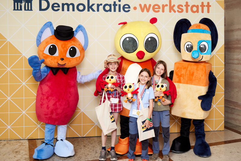 Fotopoint mit den Maskottchen der Demkratiewerkstatt und Schüler:innen