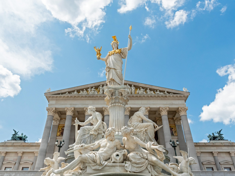 Pallas Athene steht auf einem Eulenkapitell, daneben die beiden Allegorien Vollzug der Gesetze (links) und Gesetzgebung (rechts). Die Brunnenschale aus Neuhauser Granit mit den allegorischen Personifikationen von Inn und Donau (in weiblicher Form, rechts). Geflügelte Eroten ergänzen die Darstellung. Nach einem Entwurf von Theophil Hansen