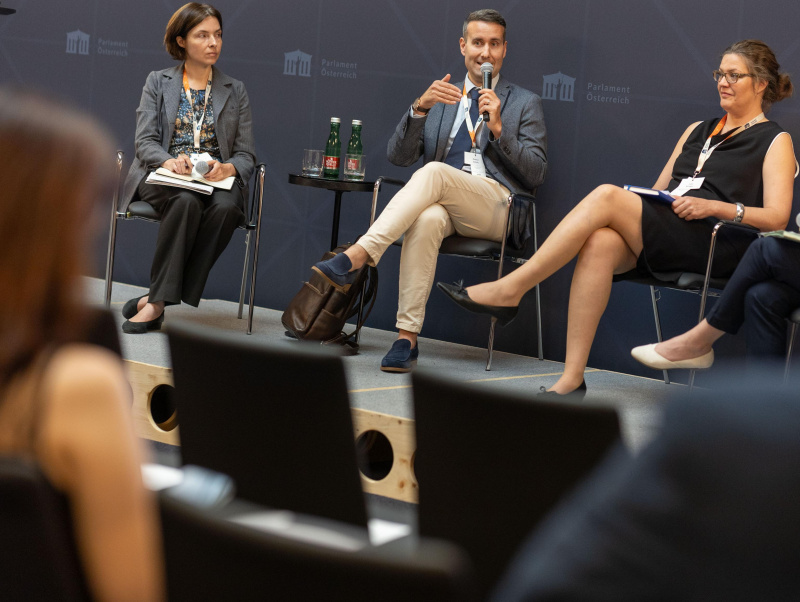 3 Teilnehmer:innen des Panel 2 sitzen am Podium, ein Teil-nehmer (Davor Jancic) spricht