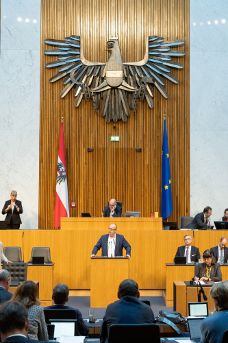 Blick Richtung Sitzungsteilnehmer:innen. Nationalratsabgeordneter Hubert Fuchs (FPÖ) am Rednerpult