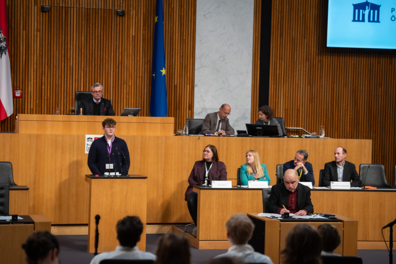 Plenarsitzung zum Abschluss des Jugendparlaments. Schüler:in am Rednerpult