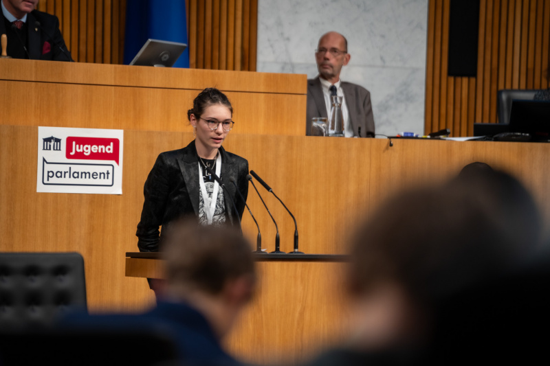 Plenarsitzung zum Abschluss des Jugendparlaments. Schüler:in am Rednerpult