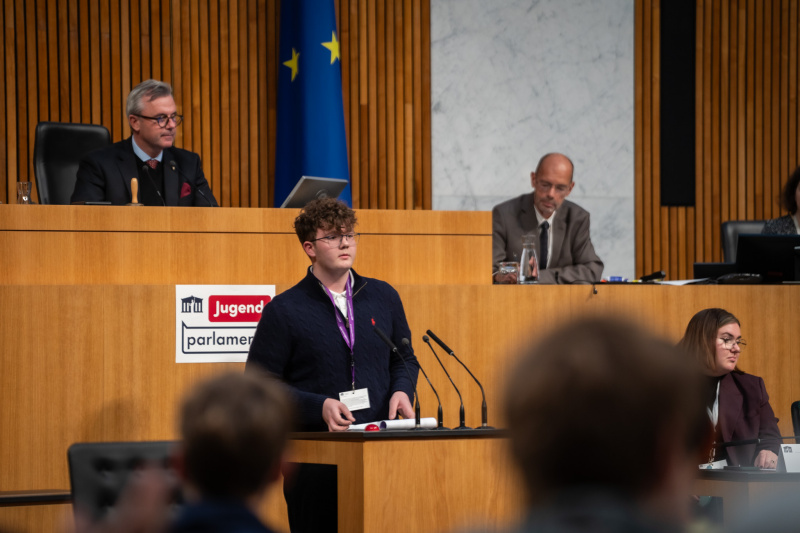 Plenarsitzung zum Abschluss des Jugendparlaments. Schüler:in am Rednerpult