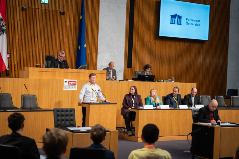 Plenarsitzung zum Abschluss des Jugendparlaments. Schüler:in am Rednerpult