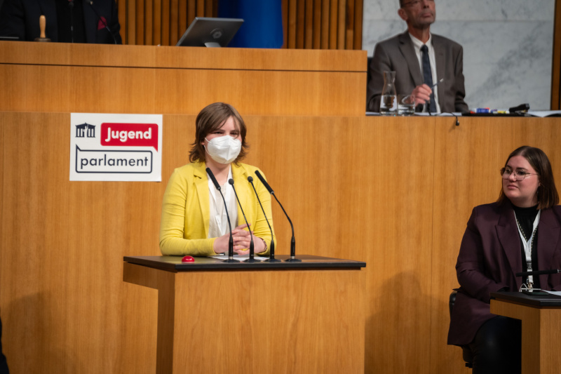 Plenarsitzung zum Abschluss des Jugendparlaments. Schüler:in am Rednerpult