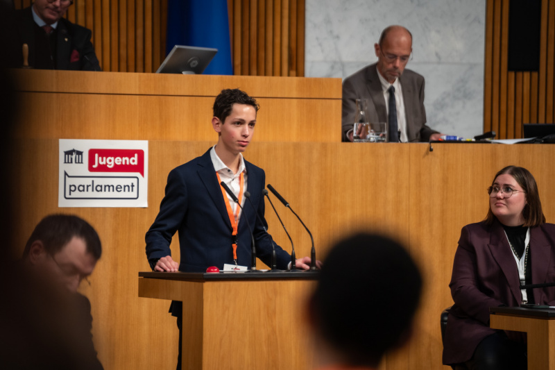 Plenarsitzung zum Abschluss des Jugendparlaments. Schüler:in am Rednerpult