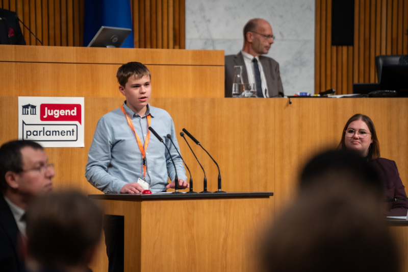 Plenarsitzung zum Abschluss des Jugendparlaments. Schüler:in am Rednerpult