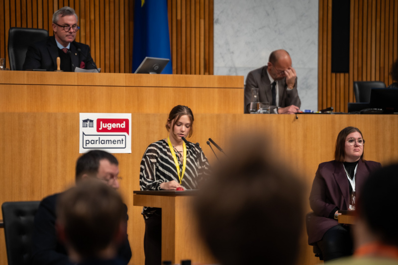 Plenarsitzung zum Abschluss des Jugendparlaments. Schüler:in am Rednerpult