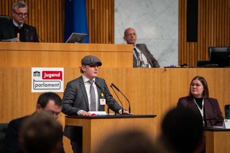 Plenarsitzung zum Abschluss des Jugendparlaments. Schüler:in am Rednerpult