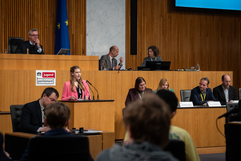 Plenarsitzung zum Abschluss des Jugendparlaments. Schüler:in am Rednerpult