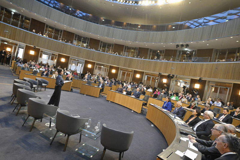 Moderation Katja Gasser. Blick Richtung Veranstaltungsteilnehmer:innen