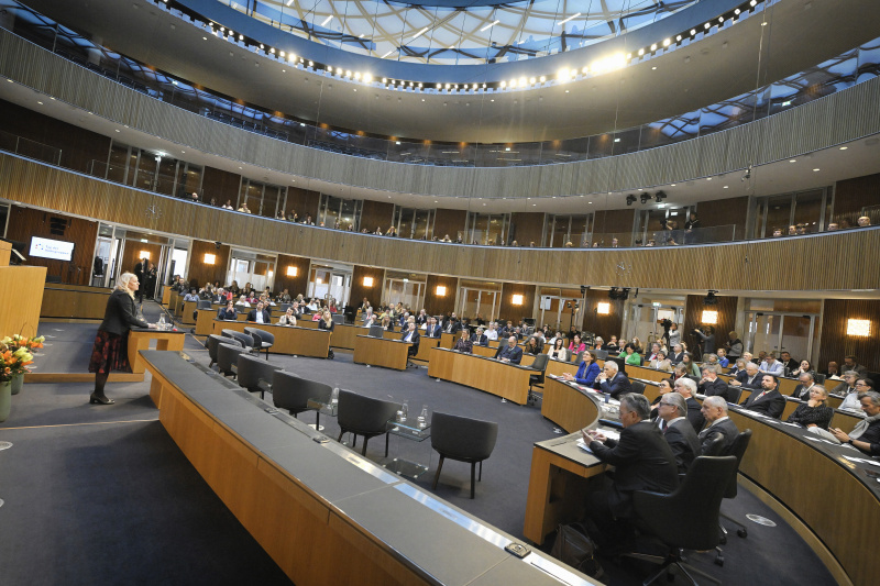 Begrüßungsworte. Bundesratspräsidentin Claudia Arpa (SPÖ). Blick Richtung Veranstaltungsteilnehmer:innen