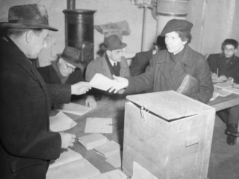 1. Nationalratswahl der 2. Republik 1945. J. Sommer mit Pressevertretern. Wählerin erhält ihr Stimmkuvert.