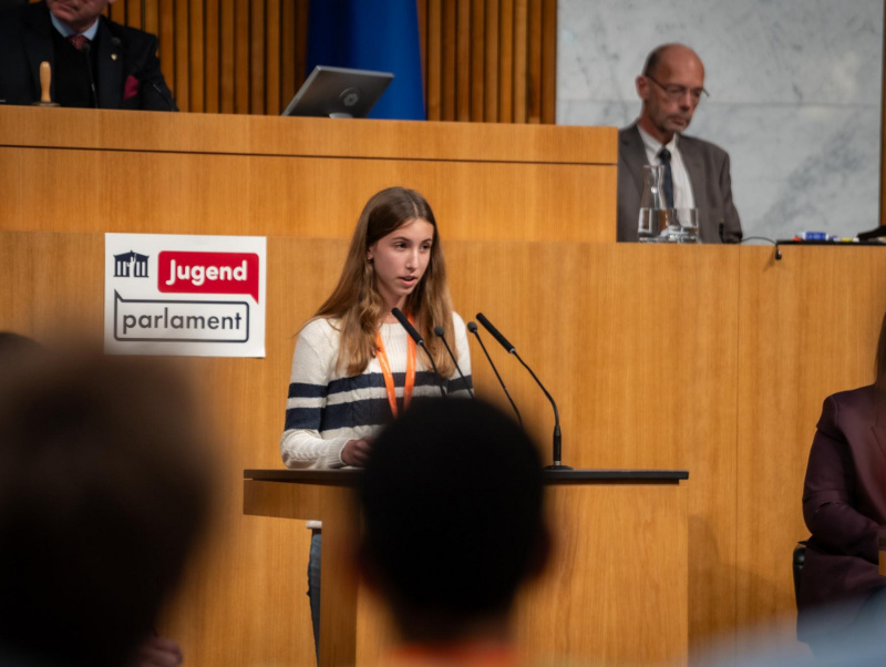 Plenarsitzung zum Abschluss des Jugendparlaments. Schüler:in am Rednerpult