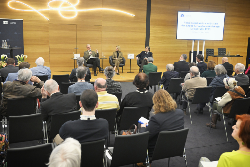 Podiumsdiskussion. Von links: Professor für Rechts- und Verfassungsgeschichte i.R., Universität Wien Thomas Simon, Moderatorin Mariella Gittler, Professor für neuere Geschichte i.R., Universität Wien.Lothar Höbelt. Blick Richtung Veranstaltungsteilnehmer:innen