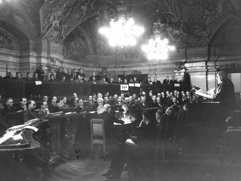 Am Rednerpult: Staatskanzler Karl Renner. Im Hintergrund Vertreter der KPÖ und ÖVP  