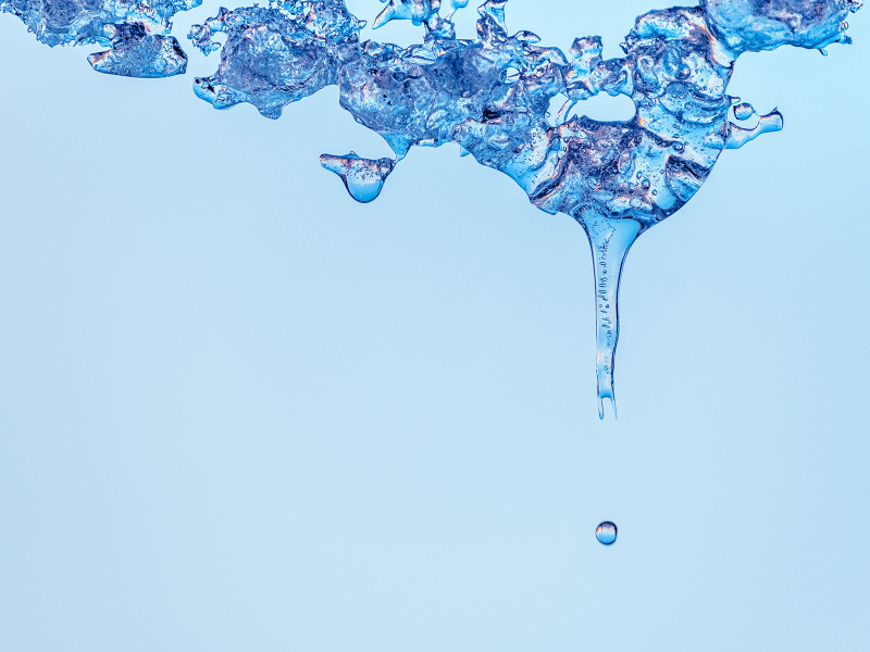Wasser, das von oben herunter tropft auf hellblauem Hintergrund.