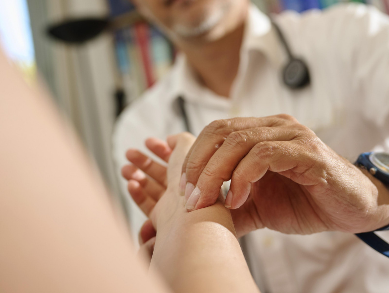 Arzt misst Puls bei einer Patientin in der Ordination