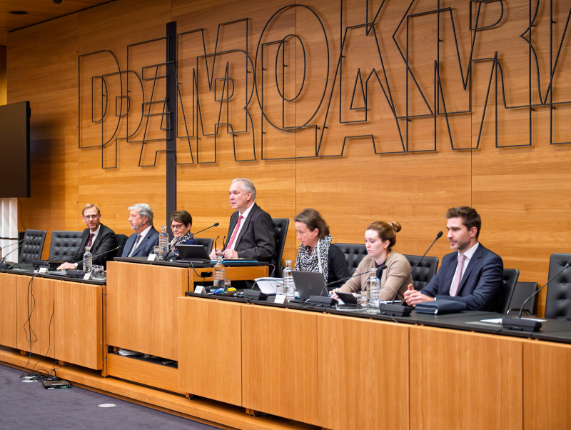 Auf dem Bild sind der Verfahrensanwalt Andreas Joklik, der stellvertretende Verfahrensrichter Wolfgang Köller, die Verfahrensrichterin Christa Edwards, der Ausschussvorsitzende Walter Rosenkranz (FPÖ) sowie Mitarbeiterinnen und Mitarbeiter der Parlamentsdirektion im Untersuchungsausschuss-Lokal zu sehen.