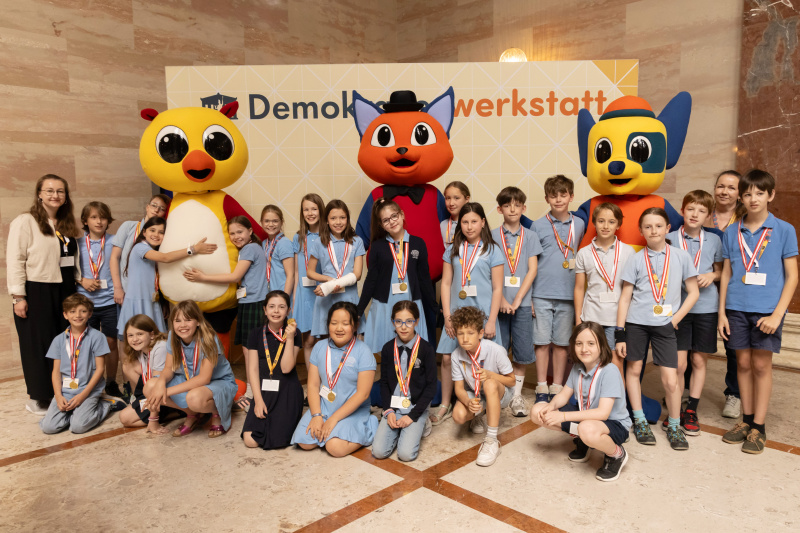 Maskottchen der Demokratiewerkstatt mit Schülerinnen und Schülern am Fotopoint in der Säulenhalle