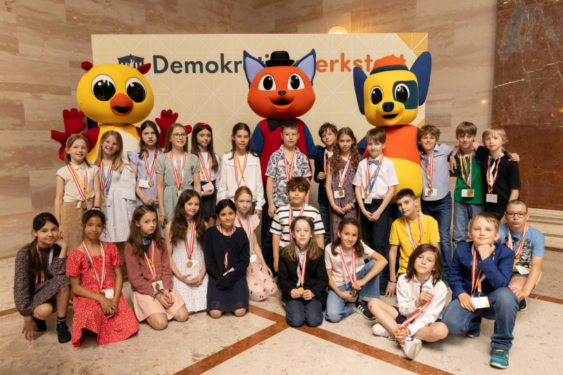 Maskottchen der Demokratiewerkstatt mit Schülerinnen und Schülern am Fotopoint in der Säulenhalle