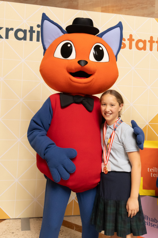 Maskottchen der Demokratiewerkstatt mit Schülerinnen und Schülern am Fotopoint in der Säulenhalle
