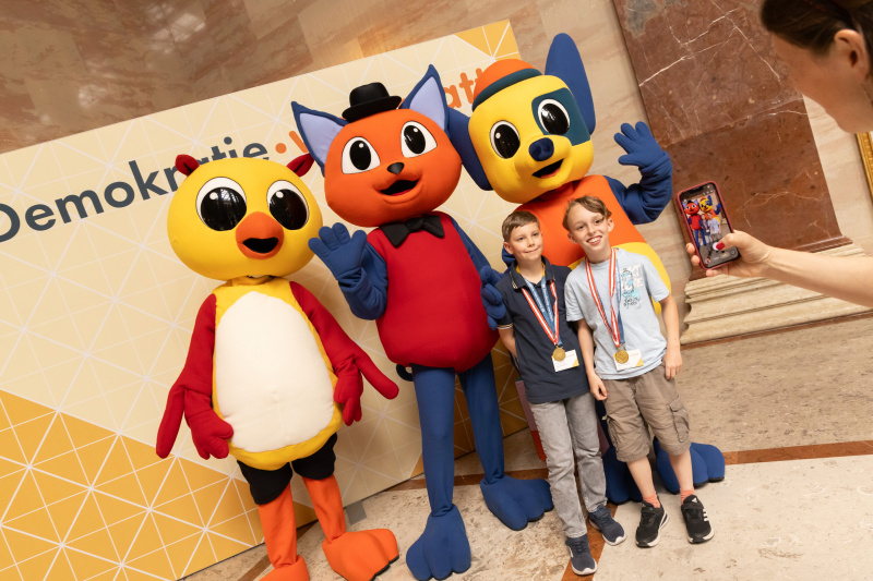 Maskottchen der Demokratiewerkstatt mit Schülerinnen und Schülern am Fotopoint in der Säulenhalle