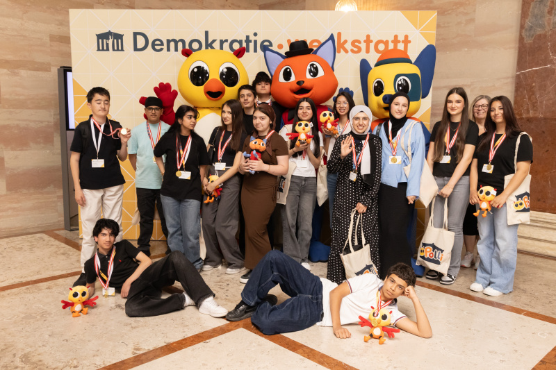 Maskottchen der Demokratiewerkstatt mit Schülerinnen und Schülern am Fotopoint in der Säulenhalle