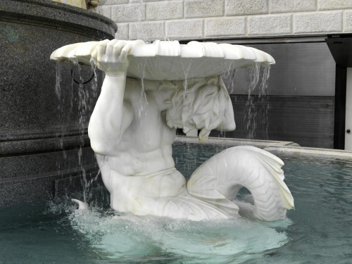 Darstellung des Triton, Meergott und auch Hilfe des Poseidon. Er krümmt sich nach vorne und hält auf den Schultern die Wasserschale. Blick in Richtung Parlamentsgebäude rechts.