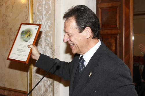 Präsident AMCHA ÖSterreich Karl Semlitsch zeigt am Rednerpult eine Auszeichnung.