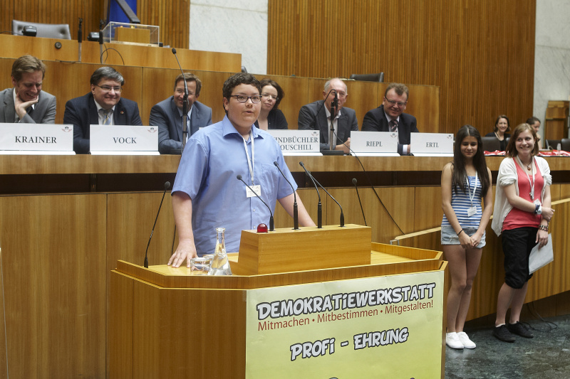 Schüler der zum Demokratiewerkstatt-Profi geehrt wird hält eine kurze Rede. Im Hintergrund auf der Regierungsbank v. links: Kai Jan Krainer - Nationalratsabgeordneter, Bernhard Vock - Nationalratsabgeordneter, Hannes Fazekas - Nationalratsabgeordneter, Tanja Windbüchler-Souschill - Nationalratsabgeordnete, Franz Riepl - Nationalratsabgeordneter und Bundesratsmitglied Johann Ertl