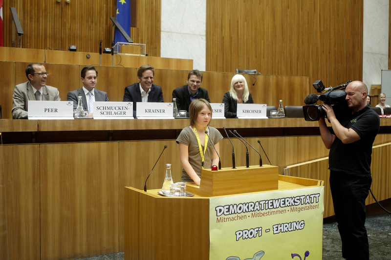 Schüler der zum Demokratiewerkstatt-Profi geehrt wird hält eine kurze Rede. Im Hintergrund auf der Regierungsbank v. li.: Mag. Bernhard Peer, Johannes Schmuckenschlager - Abgeordneter zum Nationalrat, Kai Jan Krainer - Abgeordneter zum Nationalrat, Mag. Albert Steinhauser - Abgeordneter zum Nationalrat und Elke Kirchner - Klub der Freiheitlichen