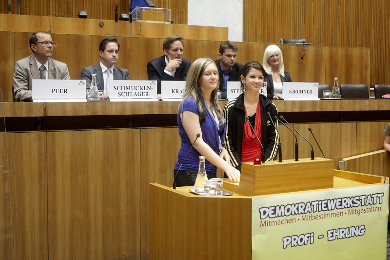 Zwei Schülerinnen die zum Demokratiewerkstatt-Profi geehrt werden halten eine kurze Rede. Im Hintergrund auf der Regierungsbank v. li.: Mag. Bernhard Peer, Johannes Schmuckenschlager - Abgeordneter zum Nationalrat, Kai Jan Krainer - Abgeordneter zum Nationalrat, Mag. Albert Steinhauser - Abgeordneter zum Nationalrat und Elke Kirchner - Klub der Freiheitlichen