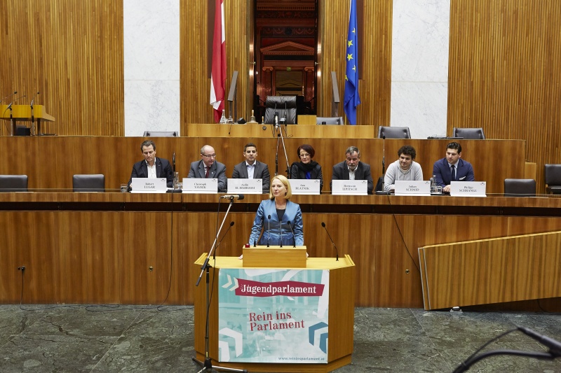 Nationalratspräsidentin Doris Bures (S) begrüßt die SchülerInnen. Am Podium v.li.: Die Nationalratsabgeordneten Robert Lugar (T), Christoph Vavrik (N) und Asdin El Habbassi (V), Bundesratspräsidentin Ana Blatnik (S) sowie die Nationalratsabgeordneten Hermann Lipitsch (S), Julian Schmid (G) und Philipp Schrangl (F)