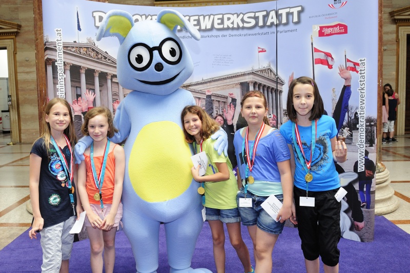 SchülerInnen mit dem Maskottchen Lesco vor dem Demokratiewerkstattplakat